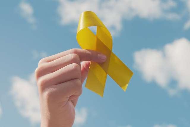 Hands holding yellow gold ribbon over blue sky