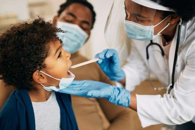 戴着口罩的非裔美国医生在一次家访中检查男孩的喉咙.