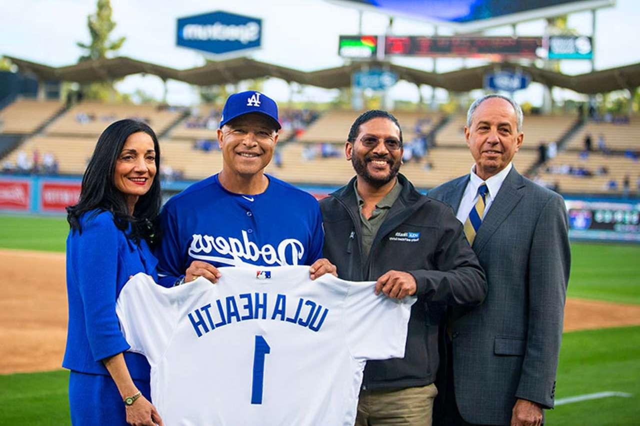 UCLA Health leaders and Dodgers coach holding a uniform with the writing that says UCLA Health 1.