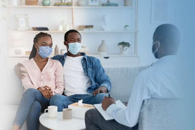 Family Therapist Talking To Black Couple Sitting In Protective Masks On Couch At Office