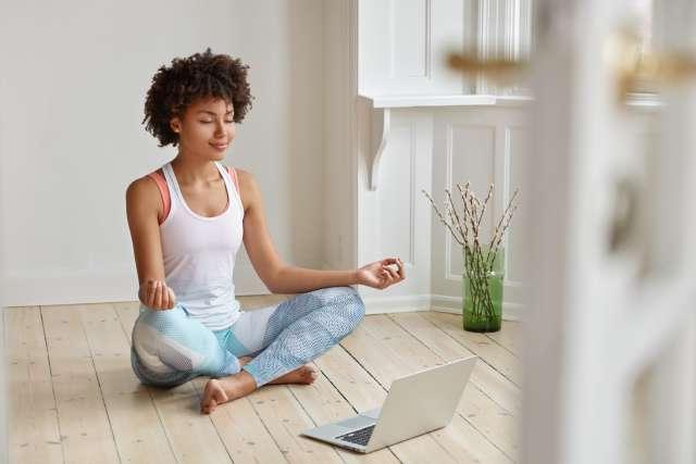 Woman meditating indoors with assistance of laptop